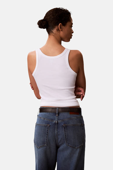 Witte Calvin Klein tanktop, geribd gebreid, gedragen met een blauwe spijkerbroek en een bruine leren riem, achtergezien.