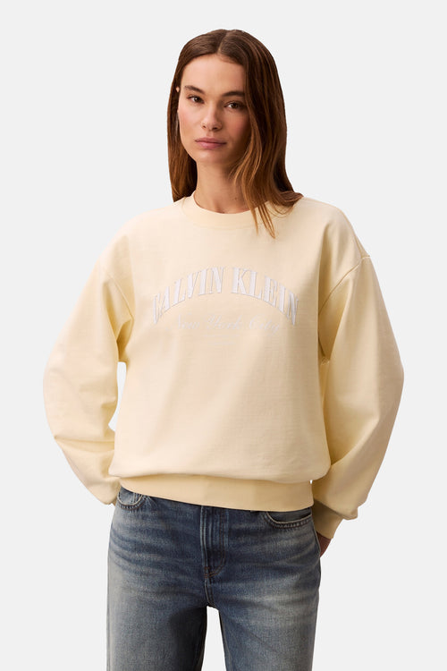 Sweat jaune col rond de Calvin Klein, porté avec un jean bleu et coupe droite.

