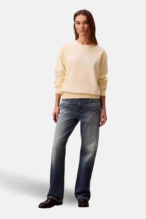 Sweat-shirt col rond jaune de Calvin Klein, porté avec un jean délavé et des mocassins en cuir.