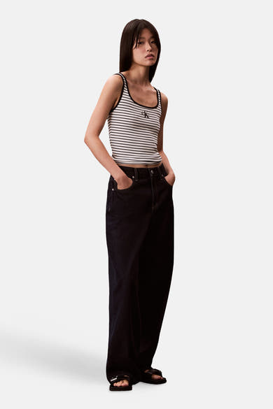 Débardeur rayé multicolore de Calvin Klein, porté avec un jean ample foncé et des sandales noires.