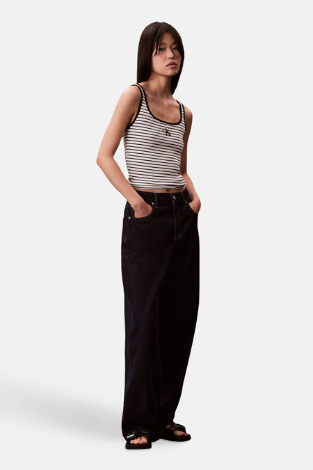 Débardeur rayé multicolore de Calvin Klein, porté avec un jean ample foncé et des sandales noires.