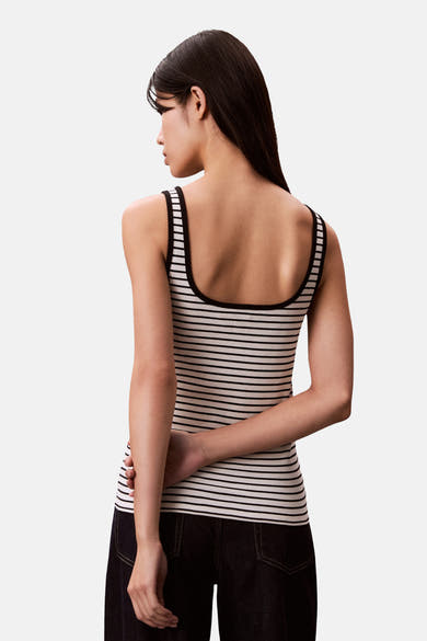 Débardeur rayé multicolore de Calvin Klein, avec dos uni visible et porté avec un jean sombre.