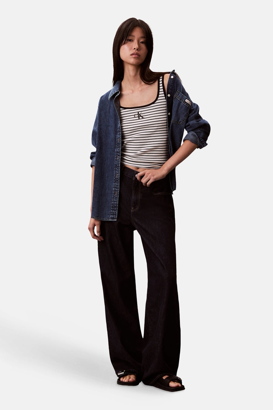 Débardeur rayé multicolore de Calvin Klein, porté avec une chemise en jean bleu délavé et un pantalon large noir.
