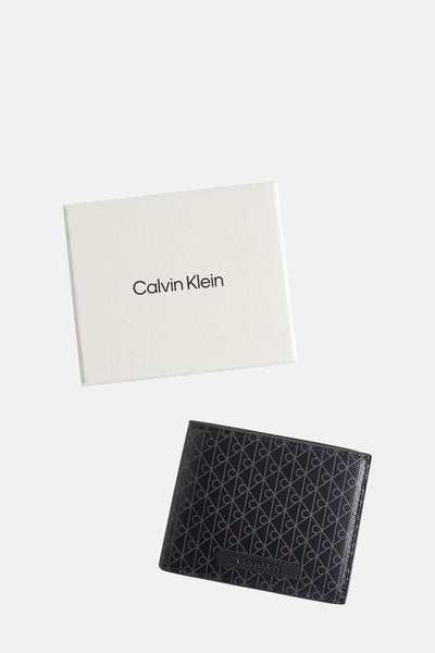 Portefeuille noir de Calvin Klein, avec motif monogramme répété et boîte d'emballage blanche.