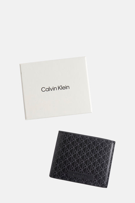 Portefeuille noir de Calvin Klein, avec motif monogramme répété et boîte d'emballage blanche.
