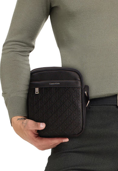 Zwarte schoudertas van Calvin Klein in leer, met reliëf geometrisch patroon en in de hand gedragen.