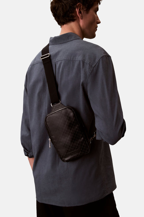 Sac à bandoulière noir de Calvin Klein avec motif géométrique porté sur le dos avec une chemise bleu-gris.
