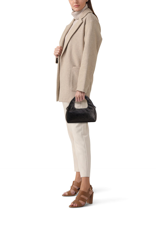 Zwarte Calvin Klein schoudertas met herhalend patroon, gedragen met een beige jas en bruine hakken.