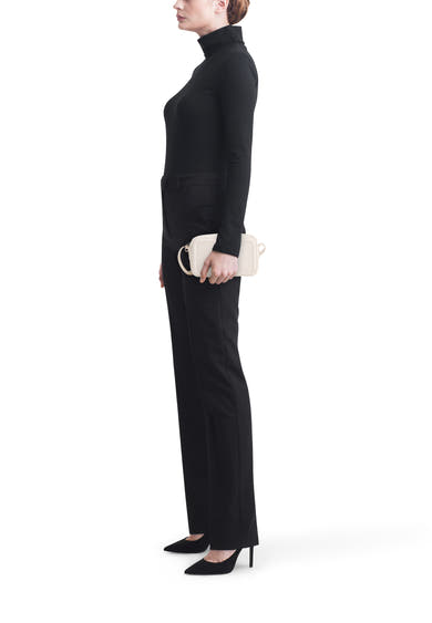 Sac à bandoulière blanc de Calvin Klein, porté avec un pantalon noir et des escarpins assortis, en vue latérale.
