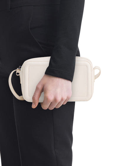 Witte Calvin Klein schoudertas, in de hand gedragen, bij een zwarte outfit.