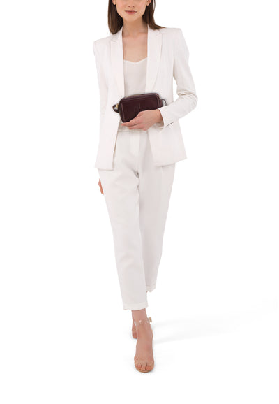 Sac à bandoulière bordeaux de Calvin Klein, porté avec un tailleur pantalon blanc et des sandales transparentes.
