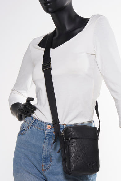 Zwarte schoudertas van Calvin Klein, gedragen door een model met een spijkerbroek en een witte blouse.
