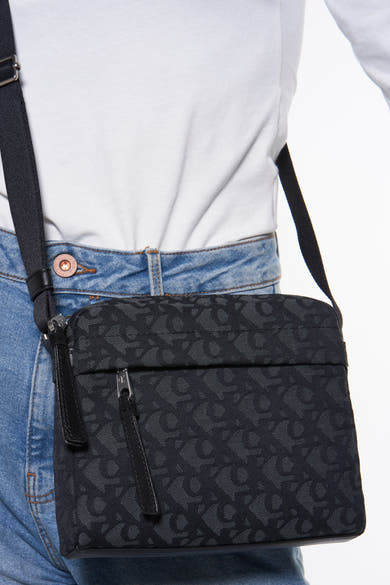 Sac à bandoulière noir de Calvin Klein, porté sur le corps, avec un motif ton sur ton.