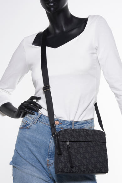 Sac à bandoulière noir de Calvin Klein avec motif logo sur mannequin portant un jean et un haut blanc.