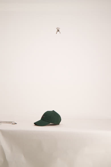 Casquette verte par Calvin Klein, posée sur une surface blanche, avec un mètre ruban à côté.
