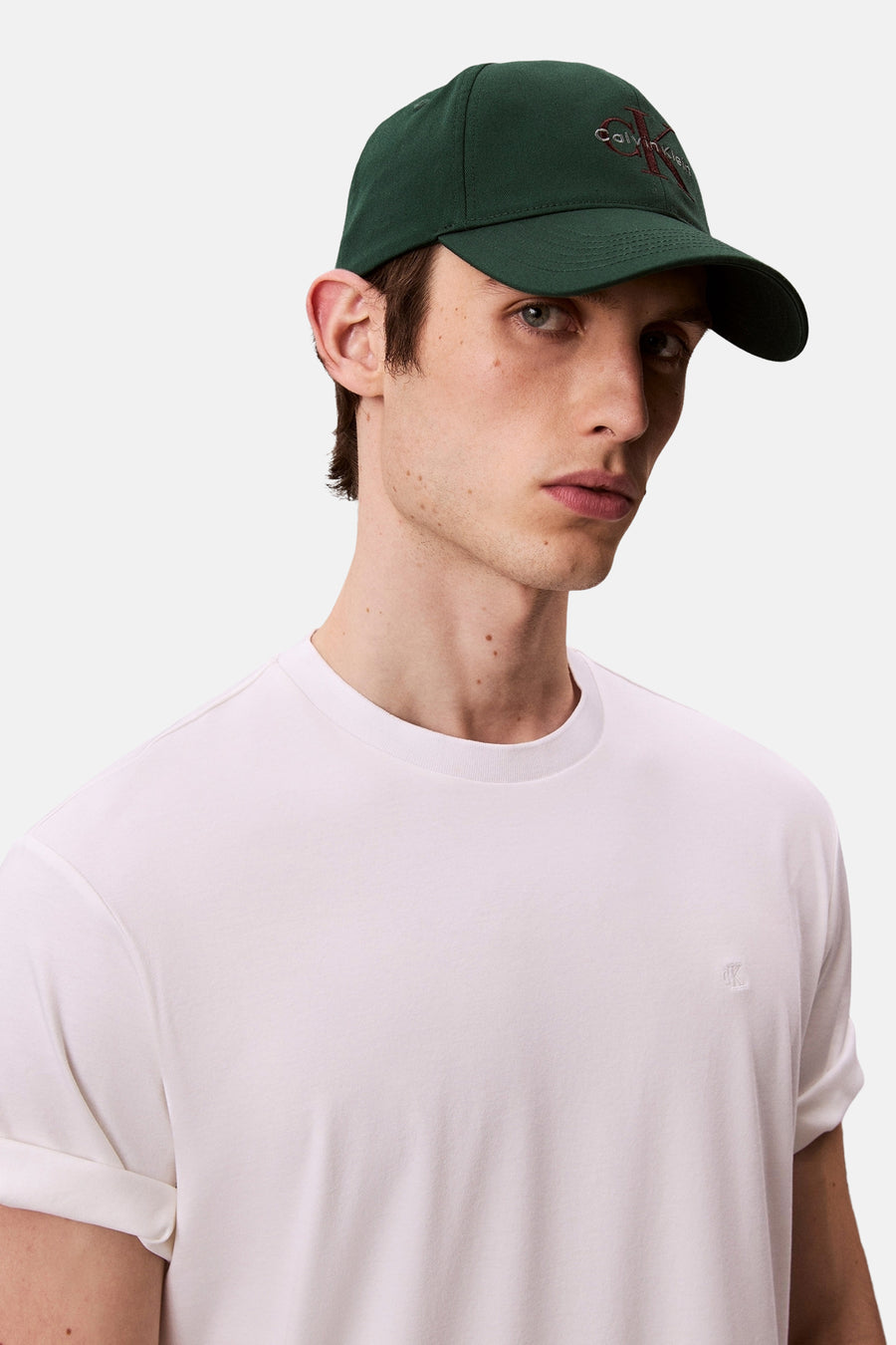 Casquette verte par Calvin Klein, portée avec un t-shirt blanc uni à manches courtes.
