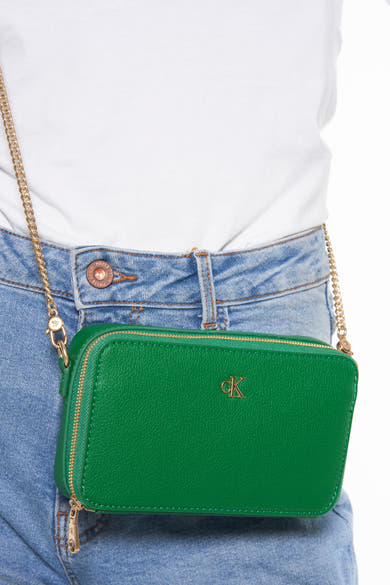 Groene schoudertas van Calvin Klein met een gouden kettingriem gedragen met een spijkerbroek en een wit T-shirt.
