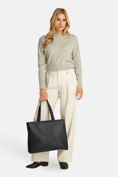 Sac à main noir de Calvin Klein, porté avec un pull gris et un pantalon taille haute couleur crème.