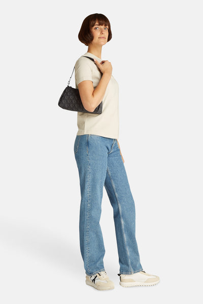 Zwarte Calvin Klein schoudertas met monogrampatroon, gedragen met een blauwe jeans en crèmekleurige sneakers.