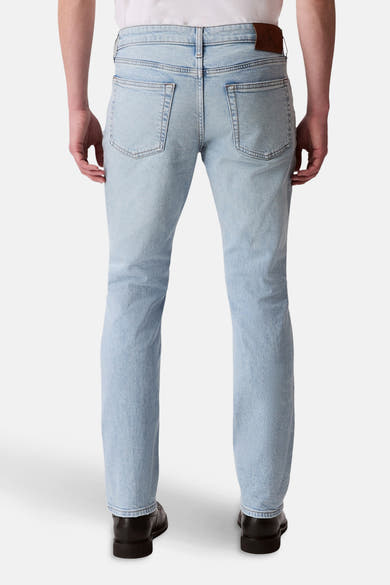 Jean slim en denim bleu clair de Calvin Klein, vue de dos, avec des poches arrières et des chaussures noires.
