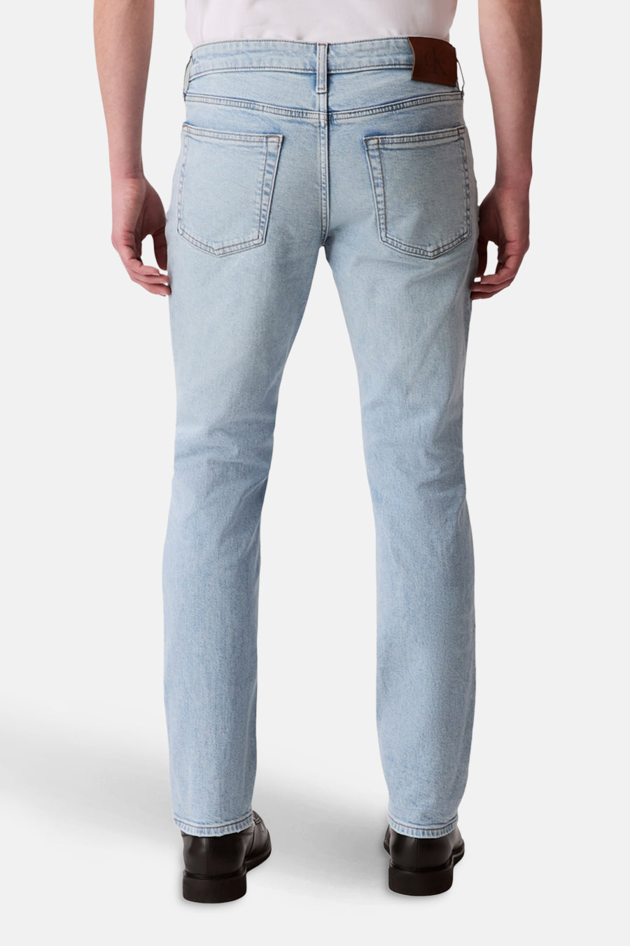 Jean slim en denim bleu clair de Calvin Klein, vue de dos, avec des poches arrières et des chaussures noires.
