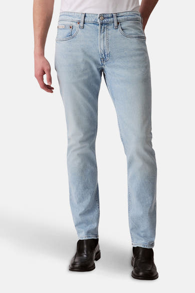 Jean slim en denim bleu clair de Calvin Klein, avec des chaussures noires.