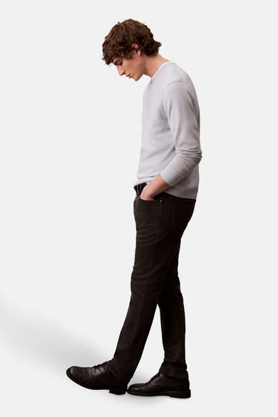 Zwarte slim fit jeans van Calvin Klein, gedragen met een lichtgrijze trui en zwarte leren schoenen, van opzij gezien.