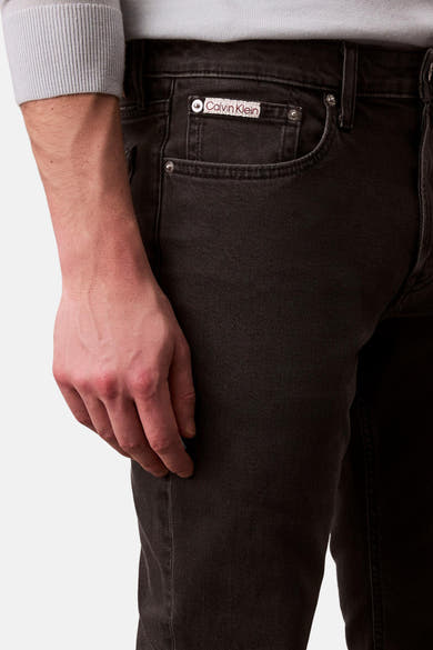 Zwarte slim fit jeans van Calvin Klein, met voorzakdetail en de hand van een man die een grijze trui draagt.