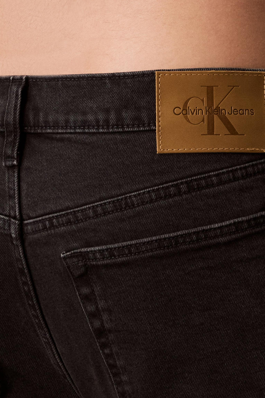 Jean tapered en denim gris foncé de Calvin Klein, avec étiquette logo en cuir marron surpiqué.