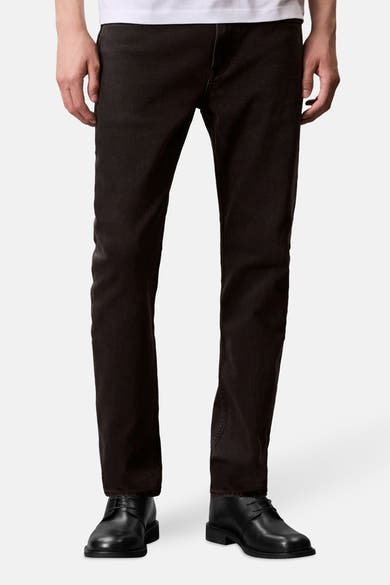 Jean fuselé en denim gris foncé de Calvin Klein, porté avec des chaussures noires à lacets.
