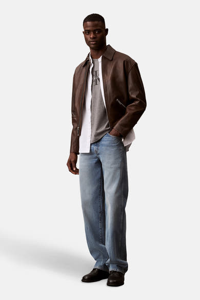 Grijs T-shirt met korte mouwen van Calvin Klein, gedragen met een bruin leren jack en een casual spijkerbroek.