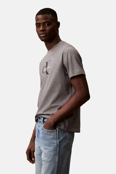 Grijs T-shirt met korte mouwen van Calvin Klein, gedragen met een lichte spijkerbroek, hand in de zak, zijaanzicht.