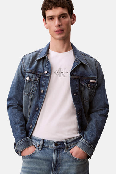 T-shirt blanc à manches courtes de Calvin Klein, porté avec une veste en jean bleu et un pantalon assorti.
