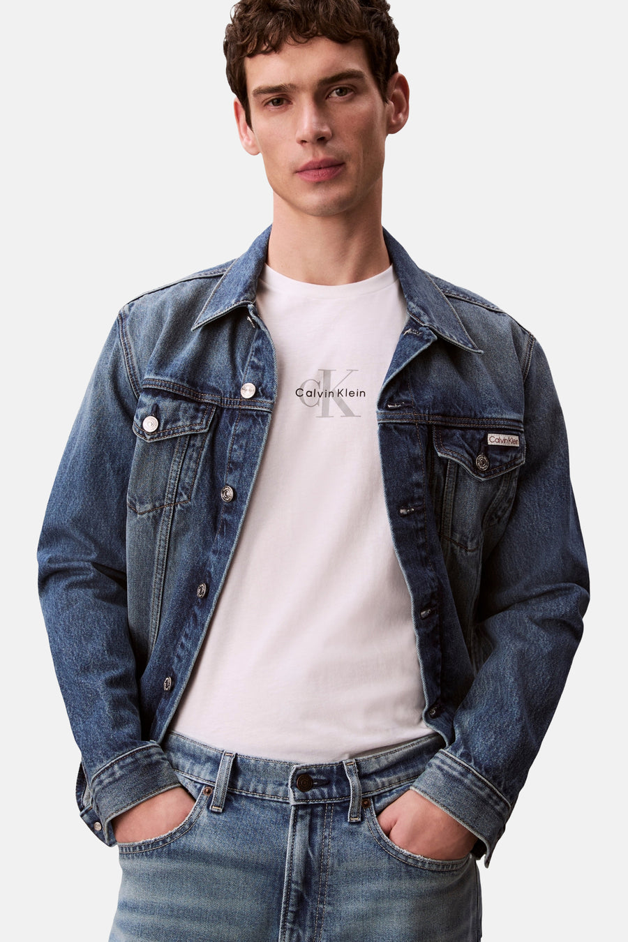 T-shirt blanc à manches courtes de Calvin Klein, porté avec une veste en jean bleu et un pantalon assorti.
