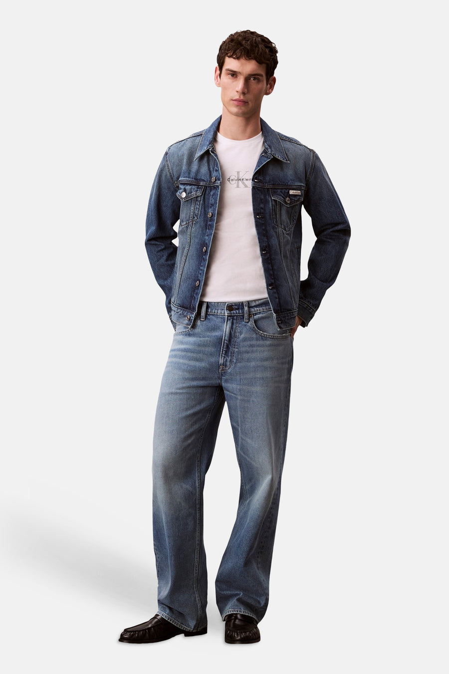 T-shirt à manches courtes blanc de Calvin Klein avec logo poitrine, porté sous une veste en jean.