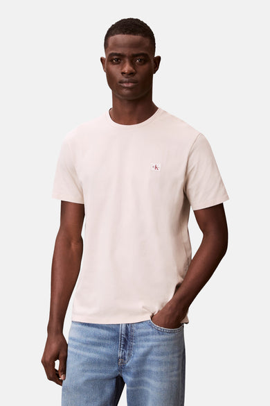 T-shirt à manches courtes écru de Calvin Klein, porté avec un jean bleu, avec logo sur la poitrine.