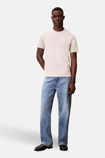 T-shirt à manches courtes écru de Calvin Klein, porté avec un jean bleu et des mocassins noirs.
