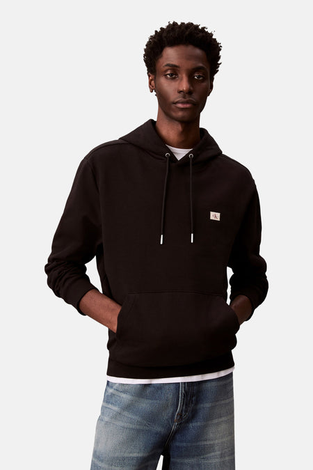 Zwarte hoodie van Calvin Klein, met trekkoord en kangoeroezak, gedragen over een blauwe jeans.