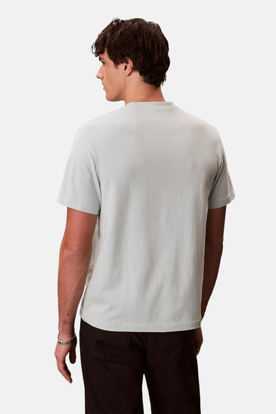 T-shirt bleu à manches courtes de Calvin Klein, porté avec un pantalon marron et un bracelet argenté, vue de dos.