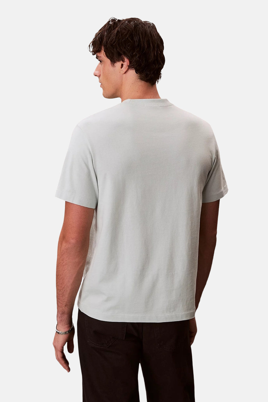 T-shirt bleu à manches courtes de Calvin Klein, porté avec un pantalon marron et un bracelet argenté, vue de dos.