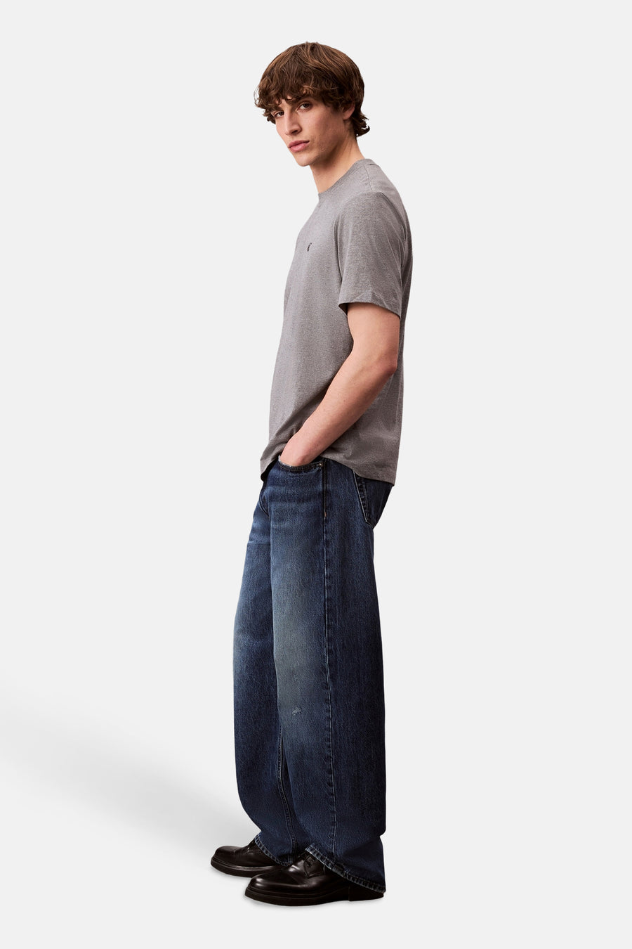 Grijs T-shirt met korte mouwen van Calvin Klein gedragen met een wijde blauwe spijkerbroek en zwarte schoenen.