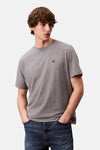 Grijs T-shirt met korte mouwen van Calvin Klein, gedragen met een donkerblauwe jeans, handen in de zakken.