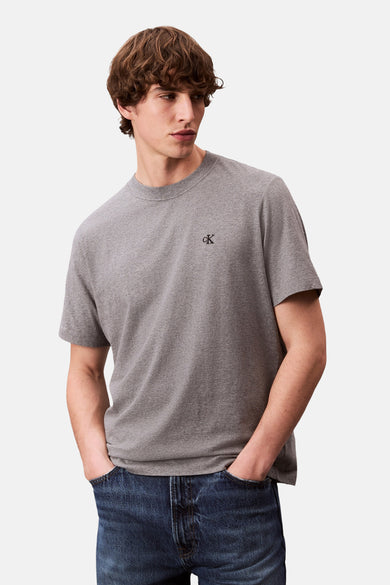 T-shirt gris à manches courtes de Calvin Klein, porté avec un jean bleu foncé, mains dans les poches.
