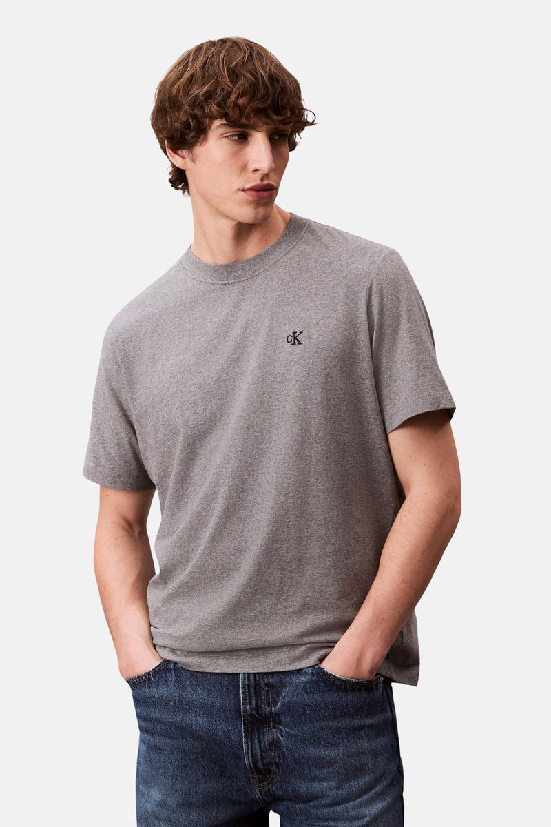 T-shirt gris à manches courtes de Calvin Klein, porté avec un jean bleu foncé, mains dans les poches.
