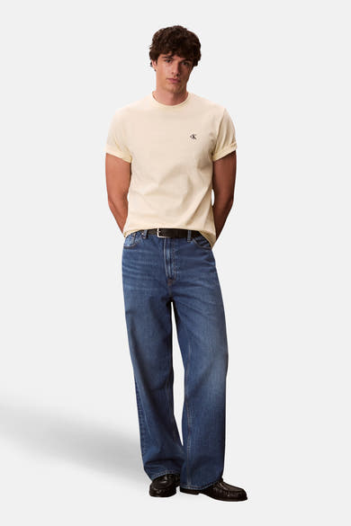 T-shirt jaune à manches courtes de Calvin Klein, porté avec un jean bleu ample et des mocassins noirs.