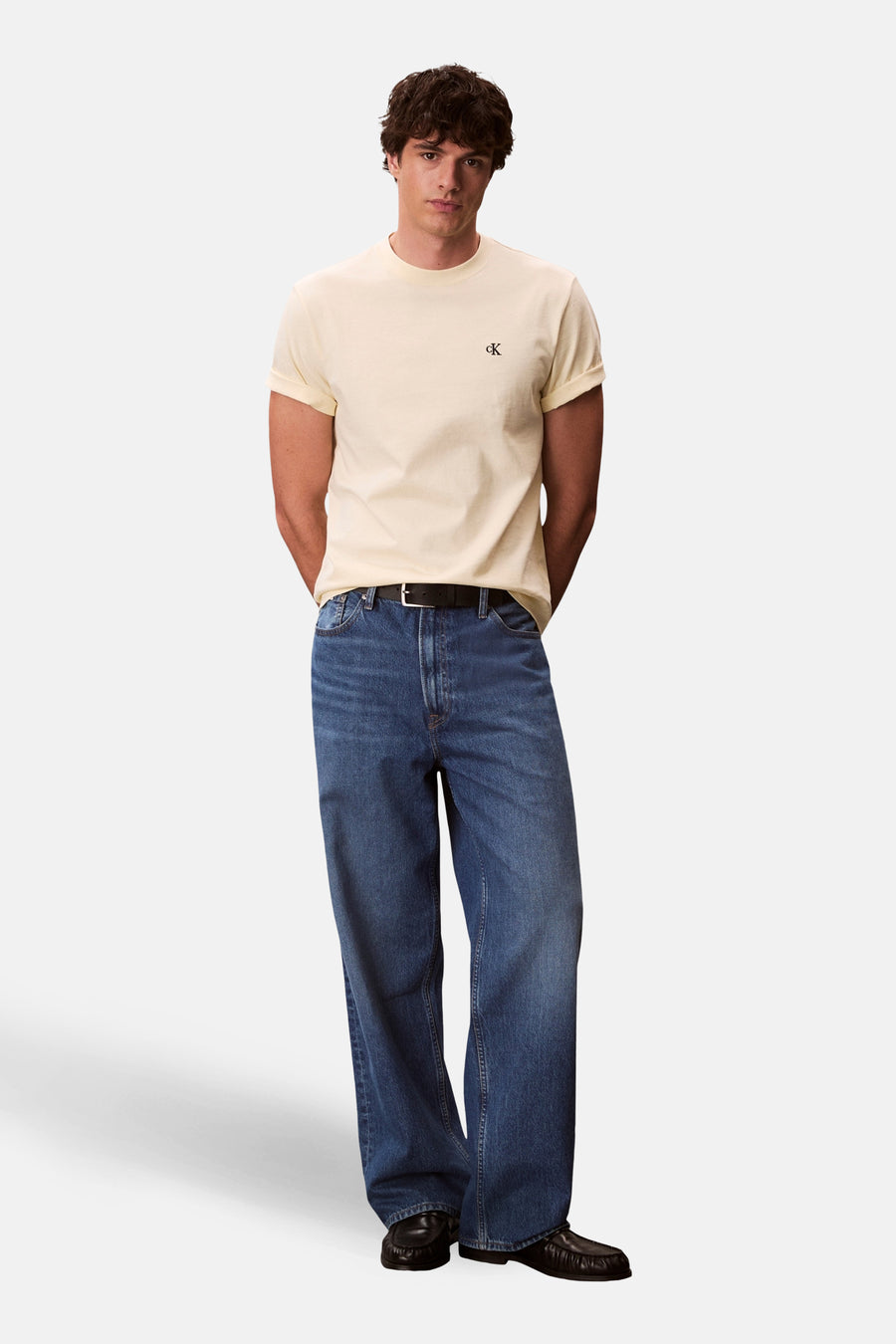 T-shirt jaune à manches courtes de Calvin Klein, porté avec un jean bleu ample et des mocassins noirs.
