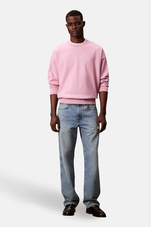 Sweat rose à col rond de Calvin Klein, porté avec un jean bleu et des mocassins noirs.
