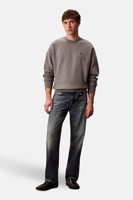 Grijze rondehals sweatshirt van Calvin Klein, gedragen met een verbleekte spijkerbroek en zwarte lage schoenen.
