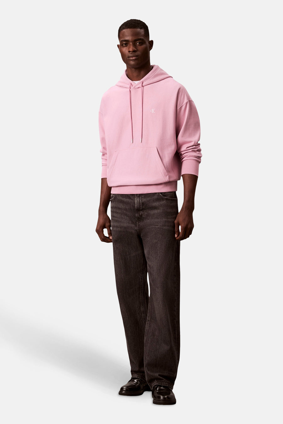 Sweat à capuche rose de Calvin Klein, porté avec un jean foncé ample et des chaussures noires.
