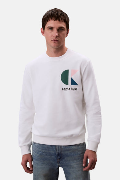 Sweat-shirt blanc de Calvin Klein, avec logo graphique coloré sur la poitrine et porté avec un jean bleu.